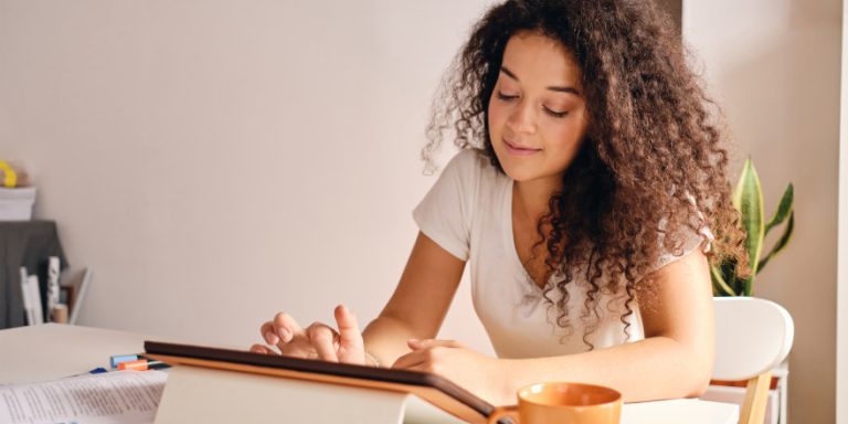 Pretty smiling girl with dark curly hair sitting at the table wi